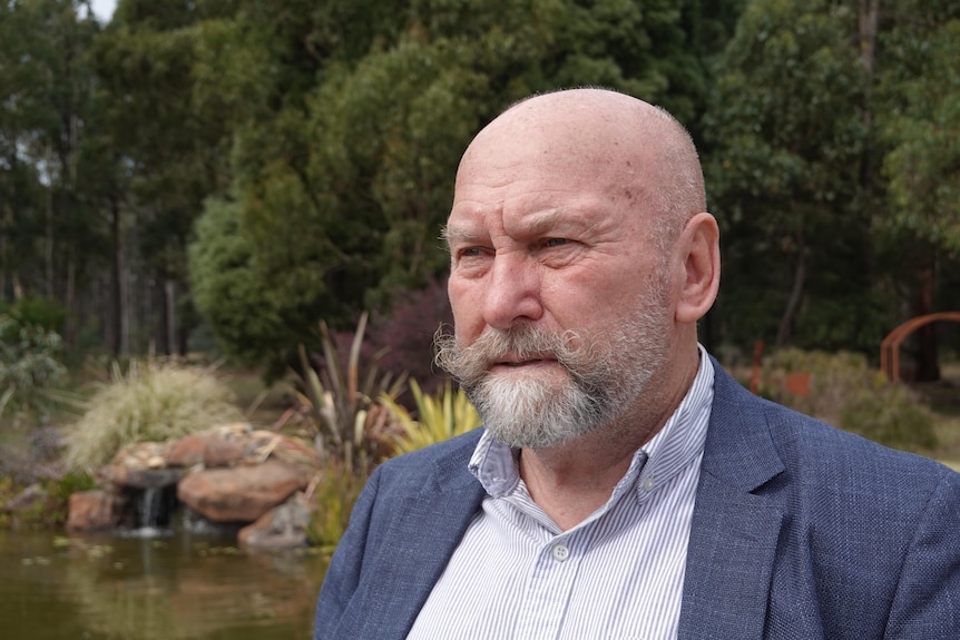 A man stands in the foreground looking into the distance, with a garden and pond behind him