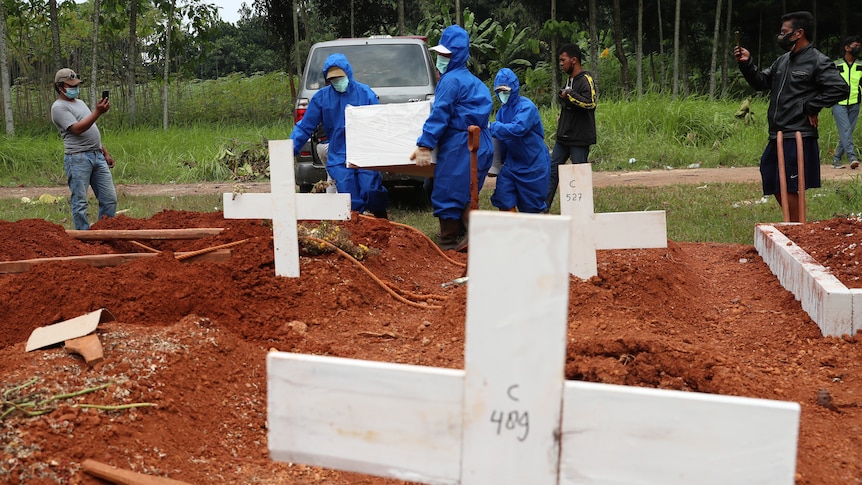 Workers in protective suits carry a coffin containing the body of a COVID-19 victim to a grave for a burial