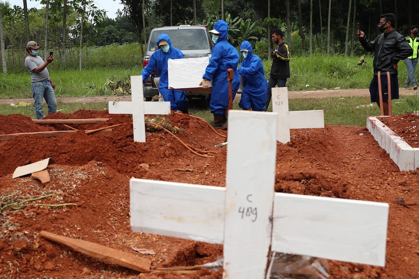 Workers in protective suits carry a coffin containing the body of a COVID-19 victim to a grave for a burial