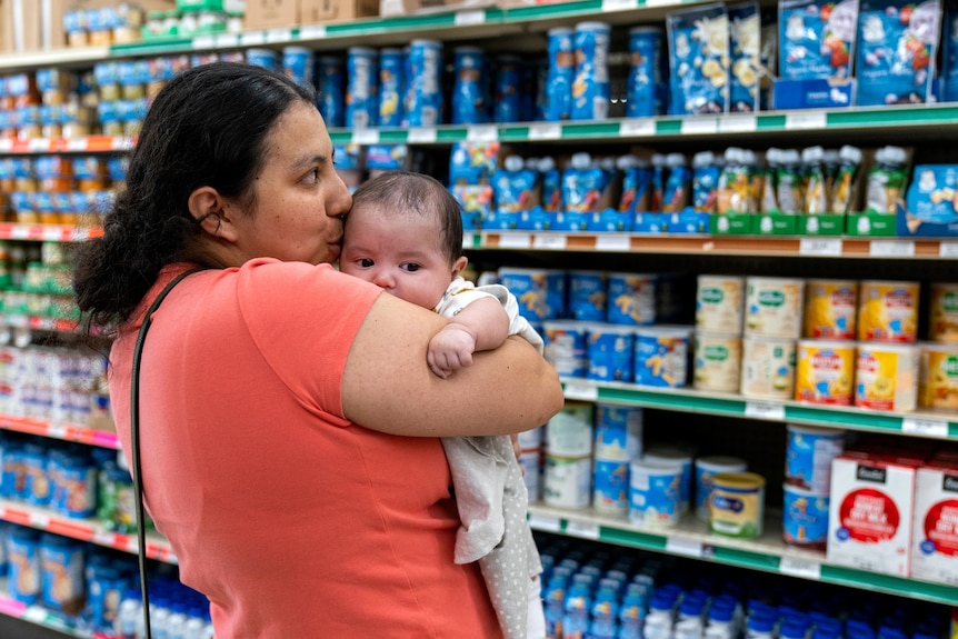 A woman holds her baby in front of baby products at a supermarket
