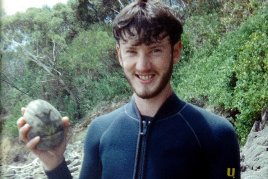 A young man in a rubber suit holding an urchin.