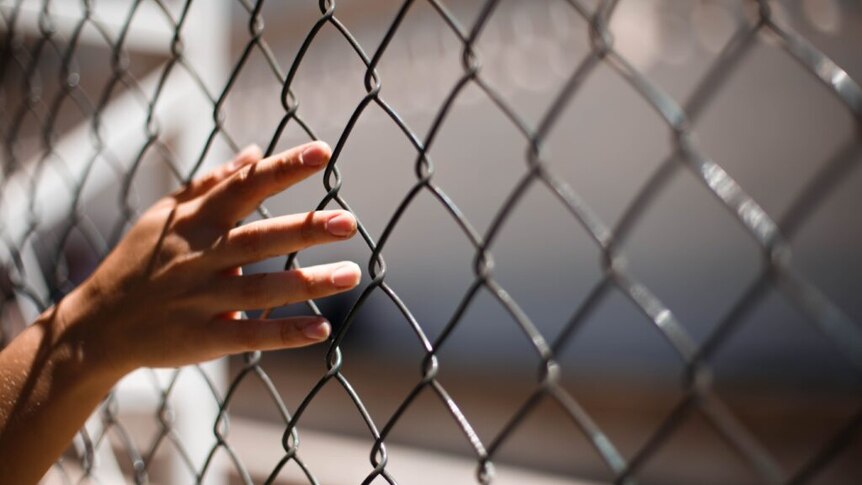 A younger person's hand trailing along a cyclone-mesh fence.