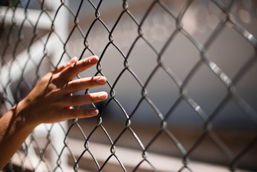 A younger person's hand trailing along a cyclone-mesh fence.