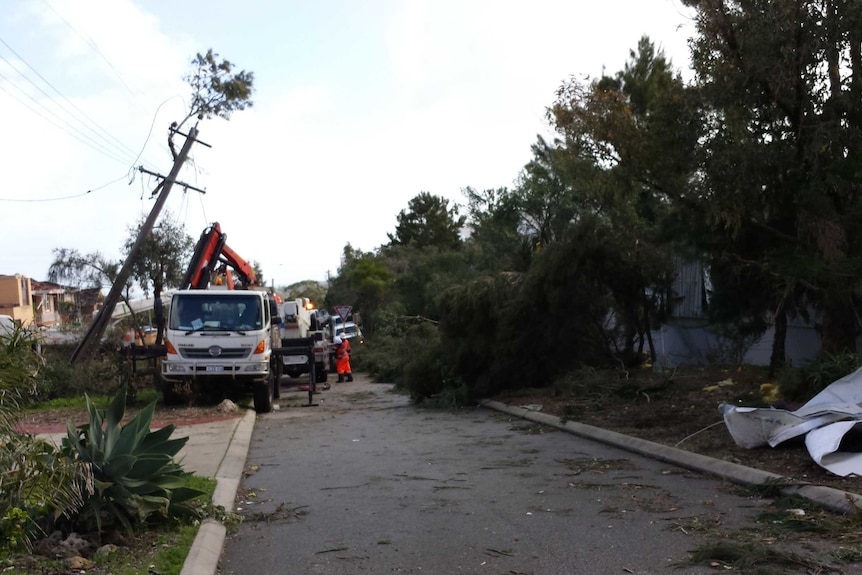 SES workers clean up on a Perth street after a tornado, with a crooked power pole and fallen trees and branches.