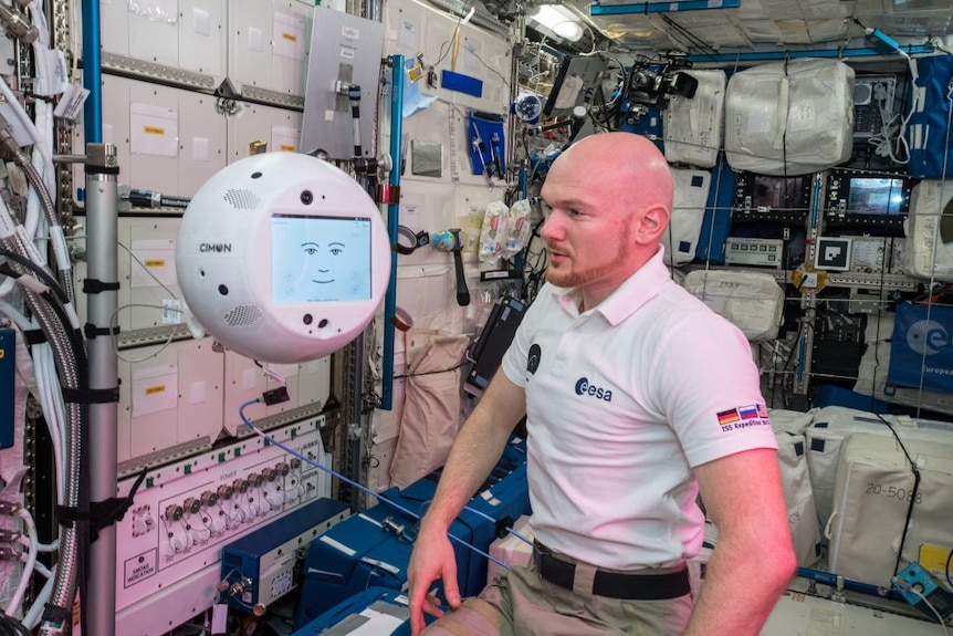 A man standing next to a free floating 3D sphere with screen displaying a face.