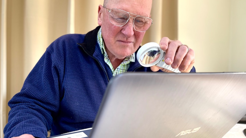 A middle-aged white man with low vision looking at a computer screen through a magnifying glass