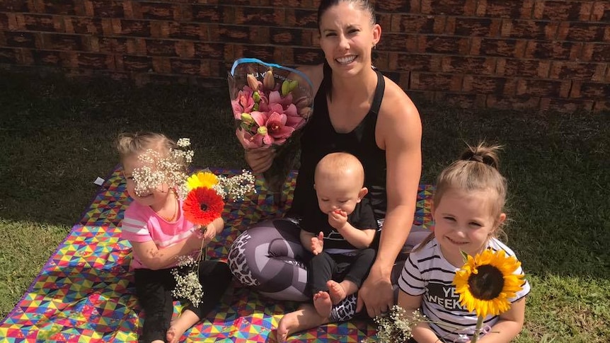 Hannah Clarke sits with her three children on a picnic rug with a fruit platter and holding flowers.