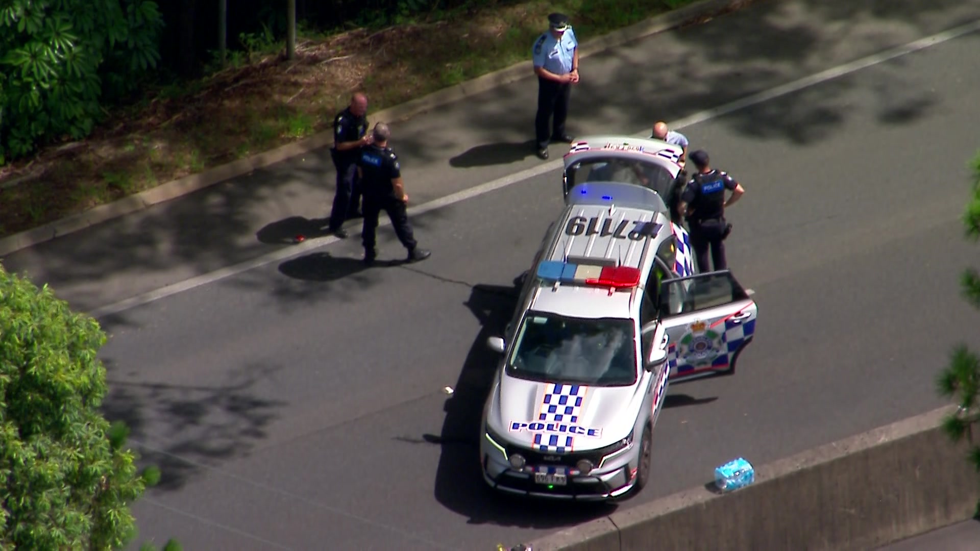 Police officers near a police vehicle parked across a rroad, as seen from above.