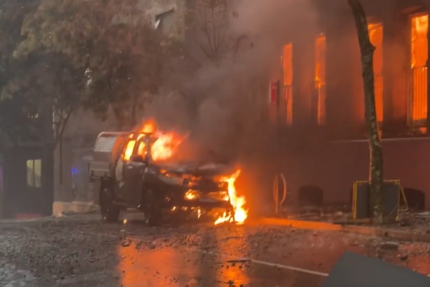 A car on fire, near a building on fire 