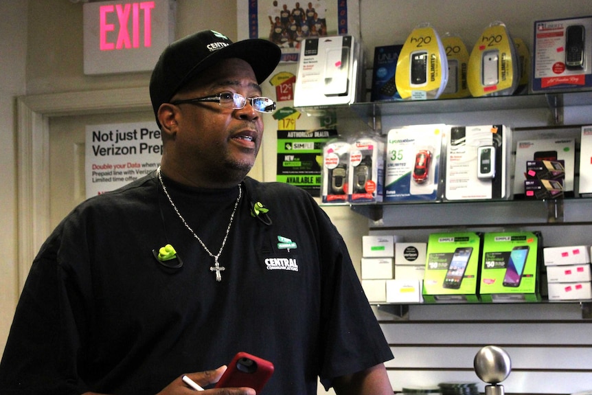 A man in a black cap and t-shirt standing in a mobile phone shop