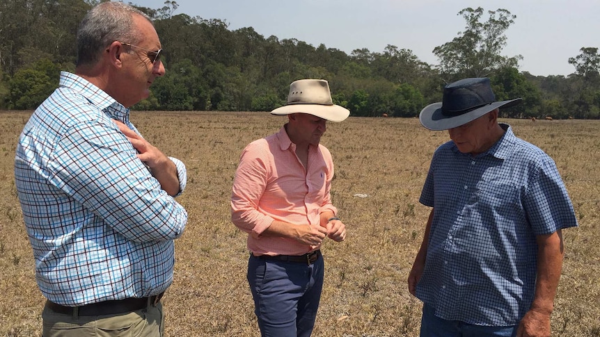 Three men inspect a drought affected property with brown grass.