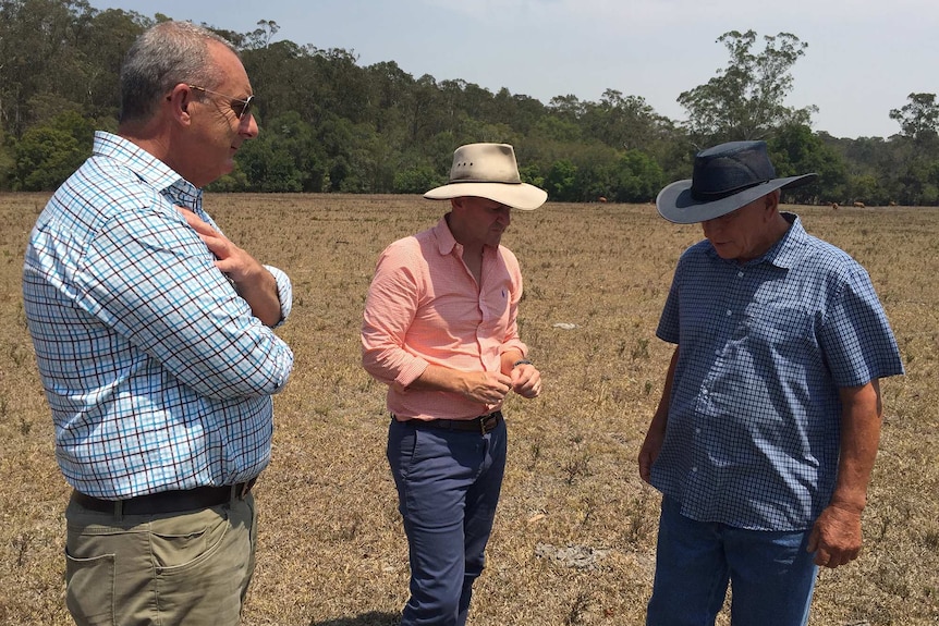 Three men inspect a drought affected property with brown grass.