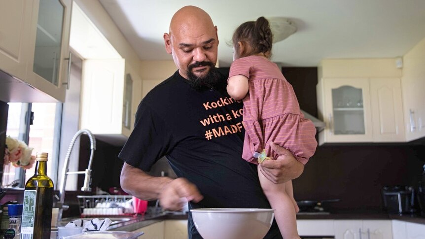 Nathan Lyons holds his young daughter while putting food ingredients in a bowl