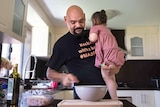 Nathan Lyons holds his young daughter while putting food ingredients in a bowl