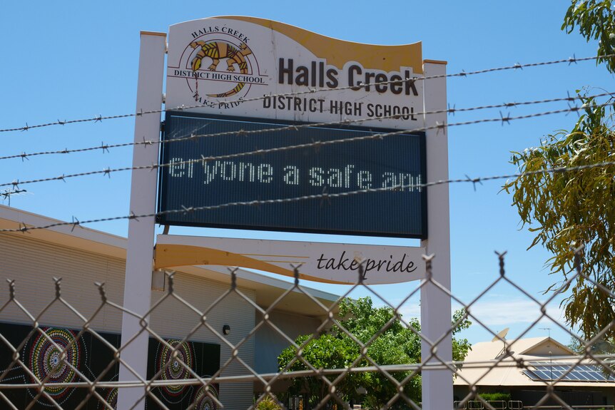 A sign that reads "Halls Creek District High school" in front of barbed wire