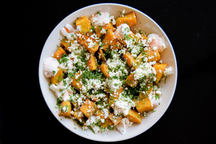 White dinner bowl filled with bright orange pumpkin chunks and topped with feta, yoghurt and dill