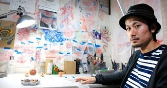 Tattoo artist Taiki Masuda sitting at a desk in his Osaka studio, surrounded by sketches and artwork.