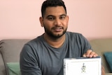 A man sits on a couch with a diploma in hand.