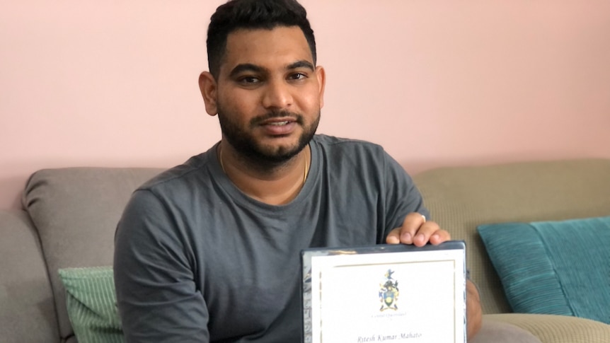 A man sits on a couch with a diploma in hand.