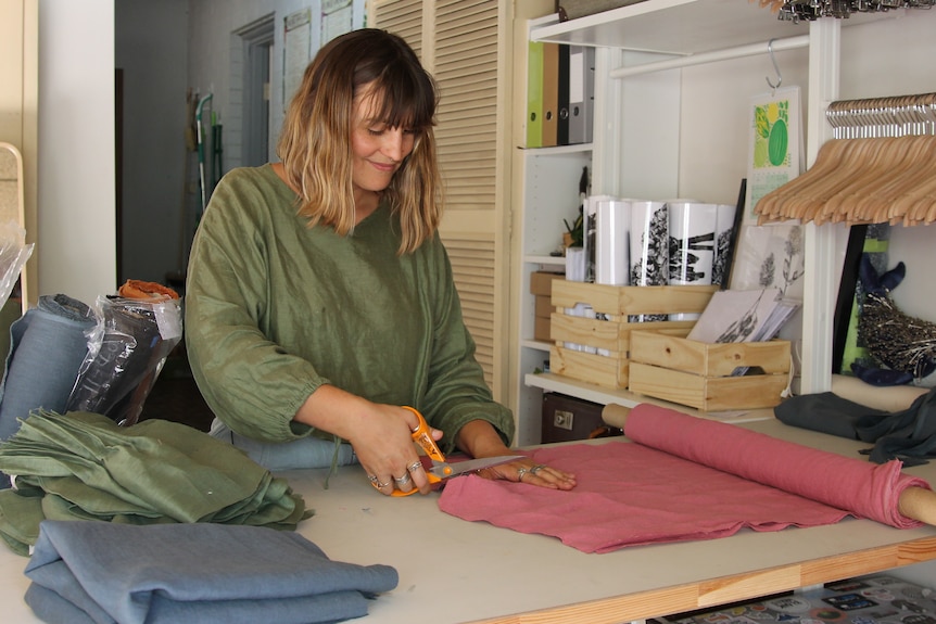 woman cutting green fabric with scissors on bench