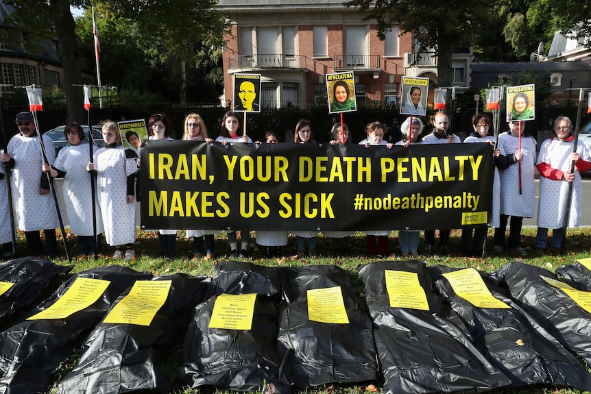 A group of people in white t-shirt gowns hold signs up with "Iran, your death penalty makes us sick"