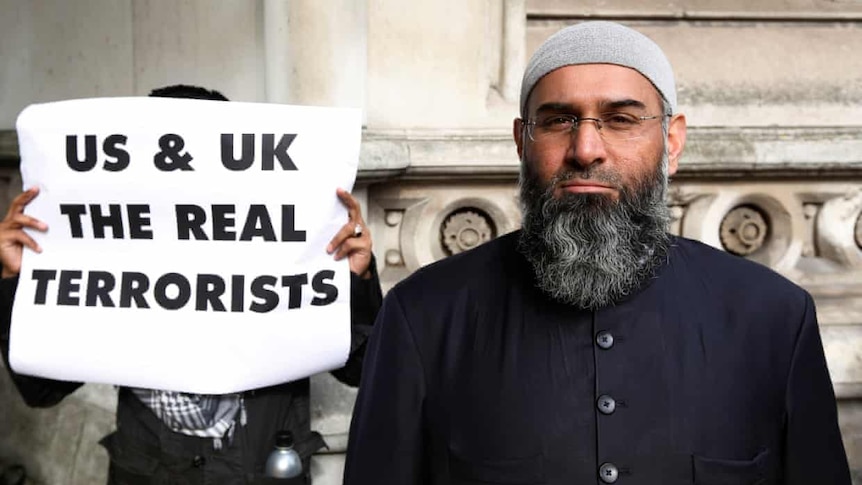 British Islamic extremist Anjem Choudary standing in front of a man holding a sign saying "US and UK the real terrorists"