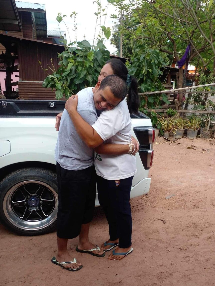 Man and woman hugging next to a white ute. 