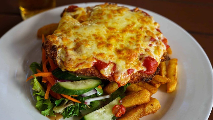 A cheese-topped chicken parmigiana with salad and fries on a plate