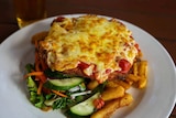 A cheese-topped chicken parmigiana with salad and fries on a plate
