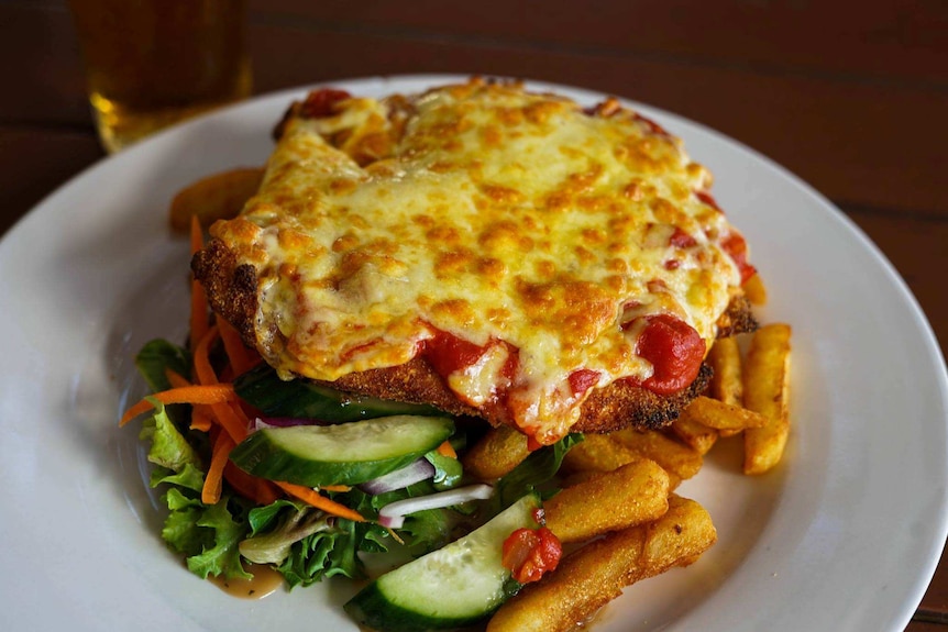 A cheese-topped chicken parmigiana with salad and fries on a plate