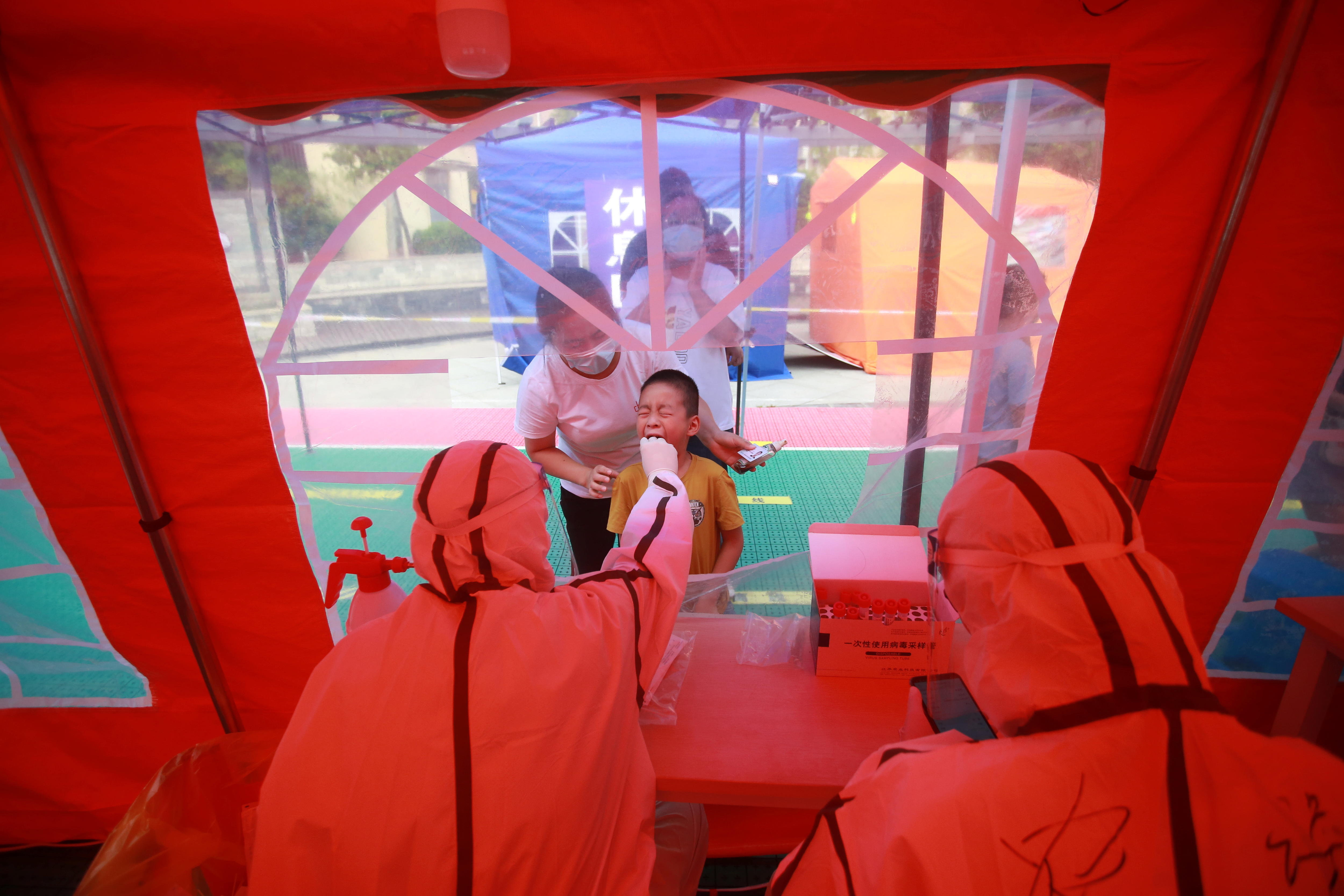 A child scrunches his face as he gets his mouth swabbed by a medical worker in PPE in Yangzhou, China
