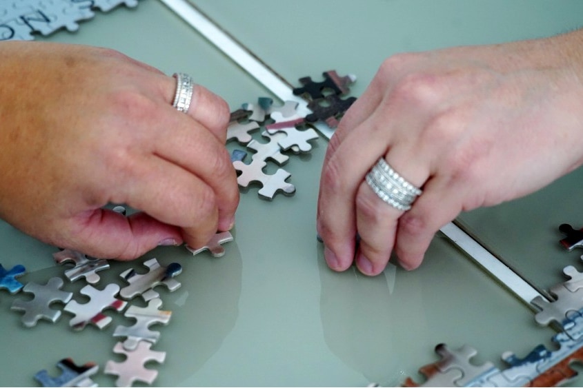 Two hands near puzzle pieces on a table, seen from close up