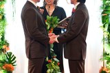 Gay men hold hands during their marriage ceremony.