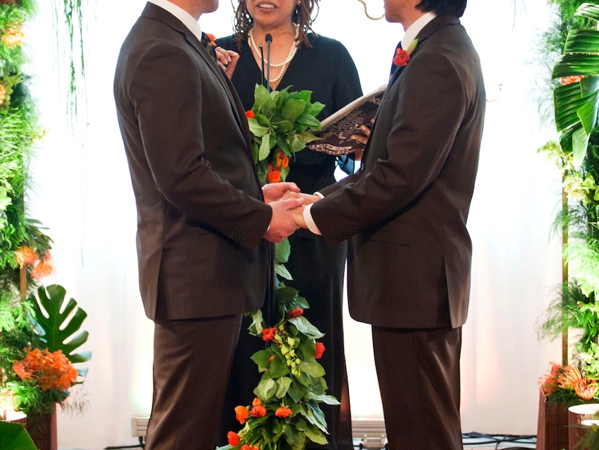 Gay men hold hands during their marriage ceremony.