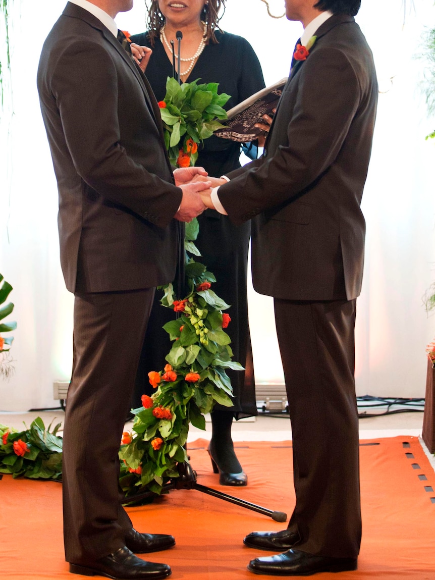Gay men hold hands during their marriage ceremony.