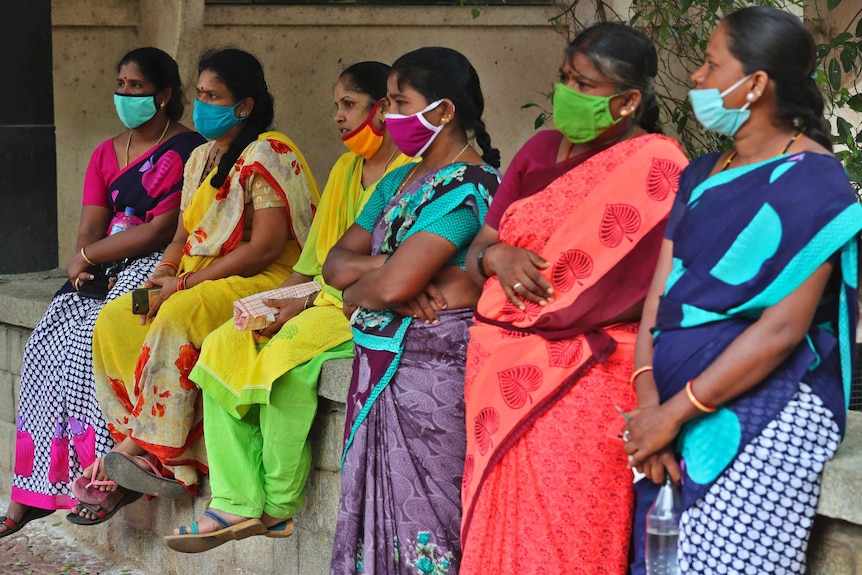A ground of women in colourful saris and facemasks.