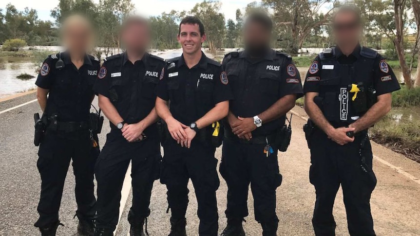 Police officers stand on a road near floodwater near Alice Springs.