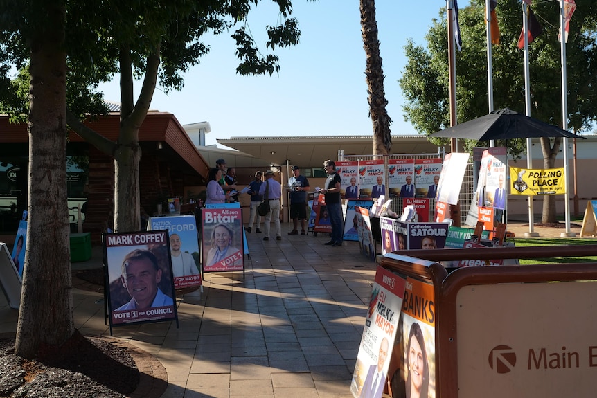 A footpath, candidates for Mayor stand on either side with signs and fliers.