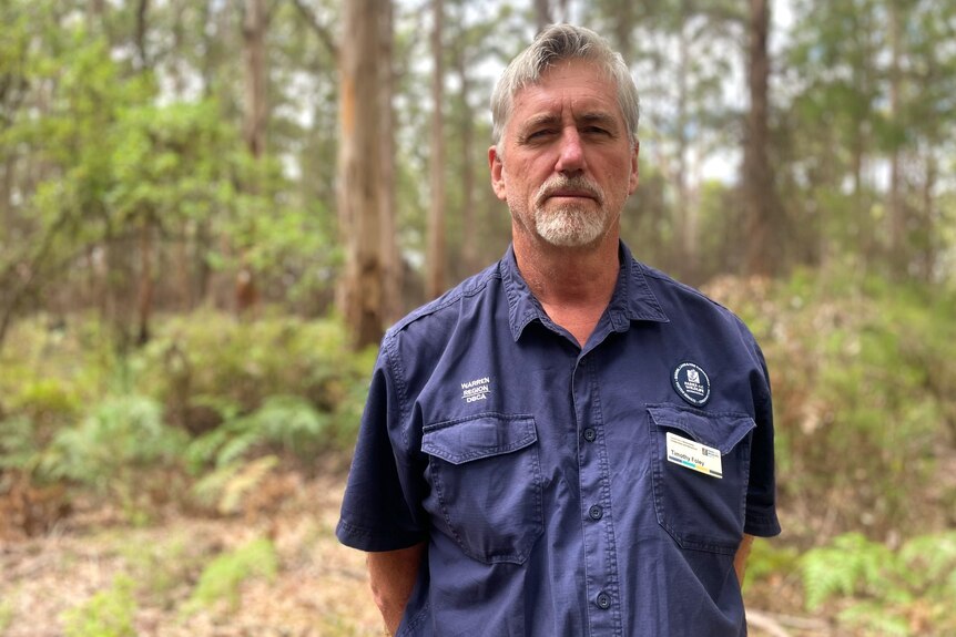 A man in a DBCA uniform in front of a forest