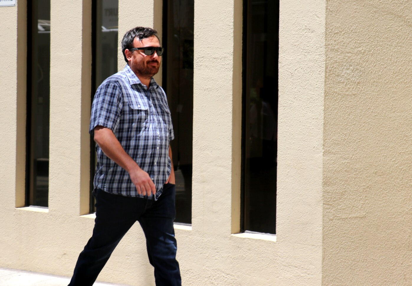 A man in a checked shirt and glasses walking outside a courthouse