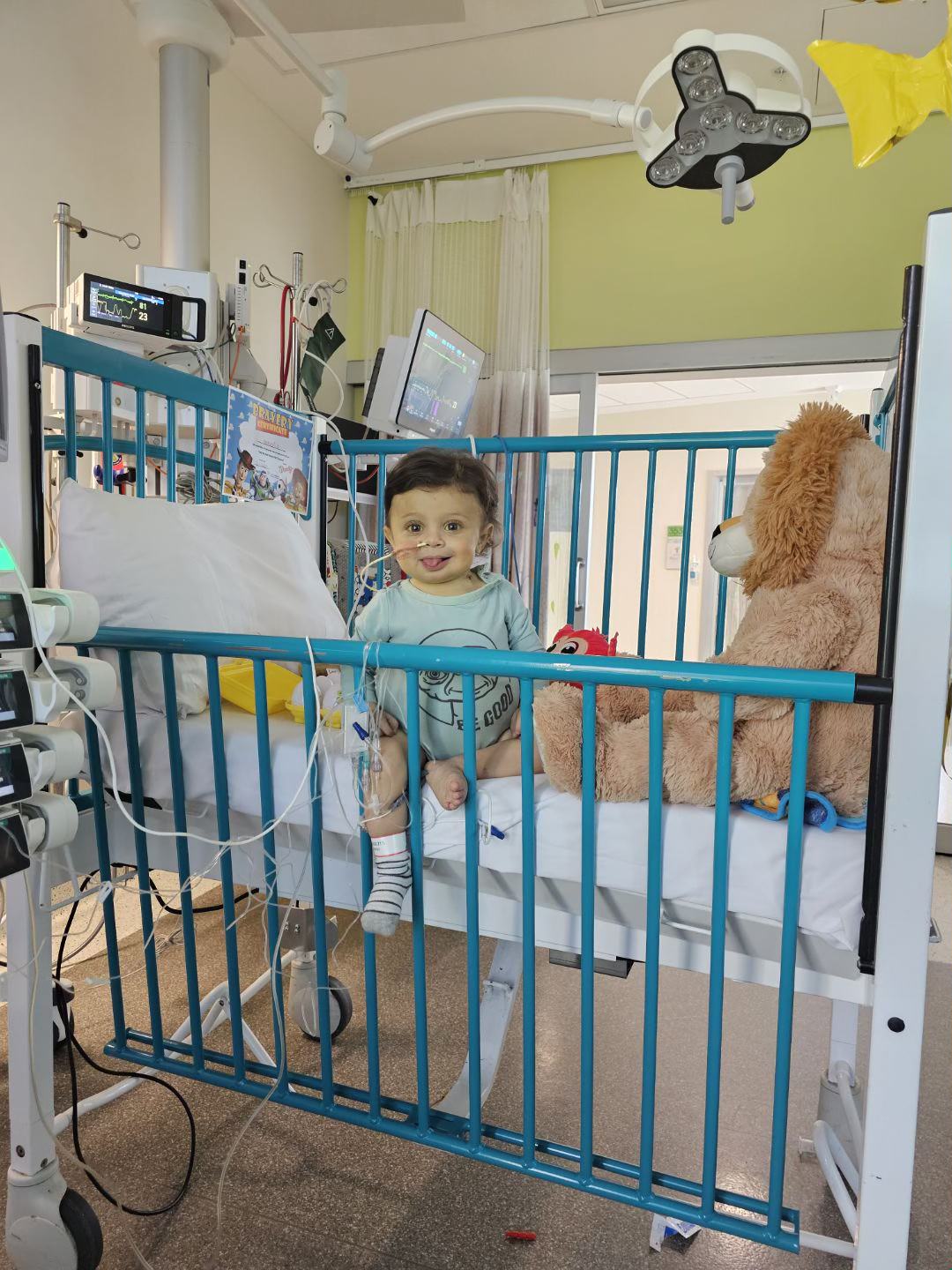 A baby boy sitting upright in a hospital bed for children with tubes fed through his nose.