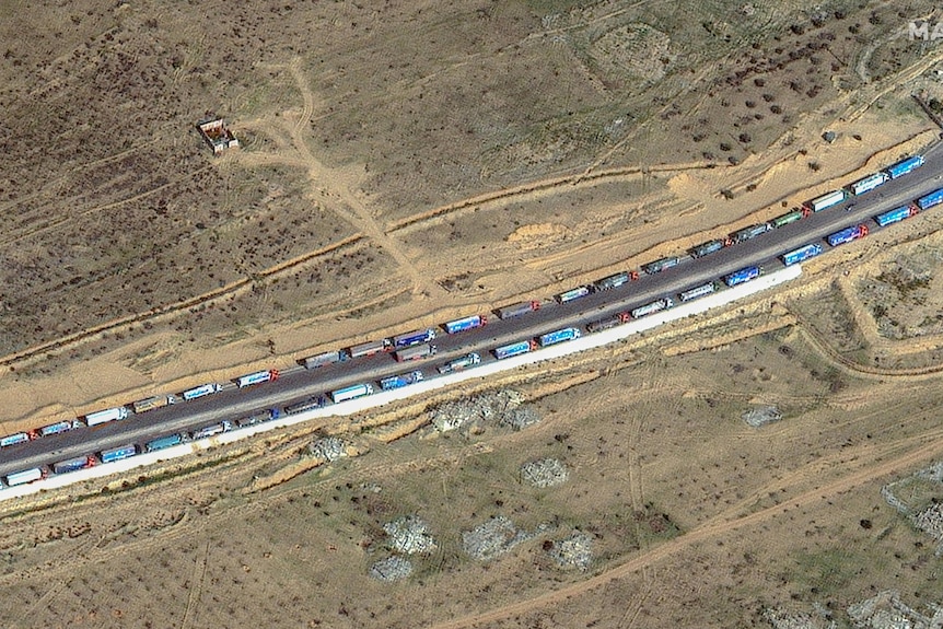 A satellite image shows two lines of trucks lined up along a desert road