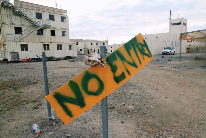 A yellow sign saying no entry with a skull attached to it stands in front of old buildings