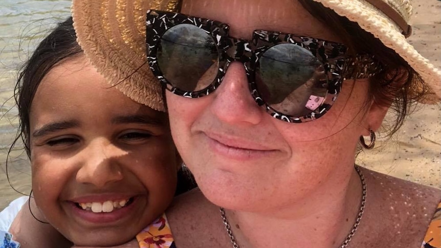 A mother and her daughter are smiling on the beach.