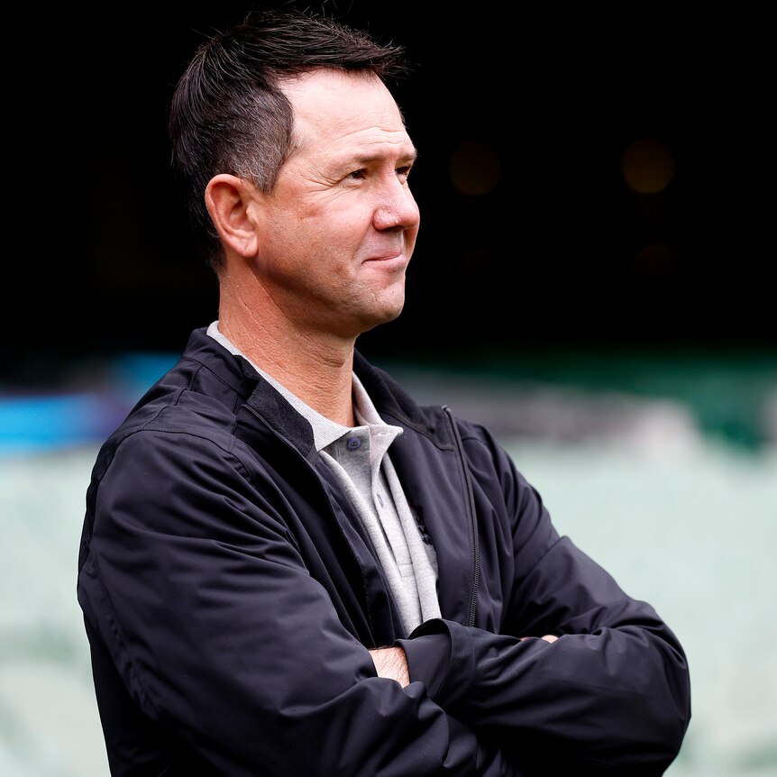 Ricky Ponting wearing a jacket folds his arms as he looks to the side of the photo