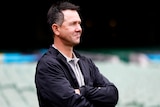 Ricky Ponting wearing a jacket folds his arms as he looks to the side of the photo