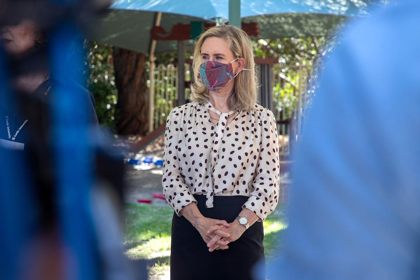 A woman wearing a mask flanked by out of focus shoulders of two people.