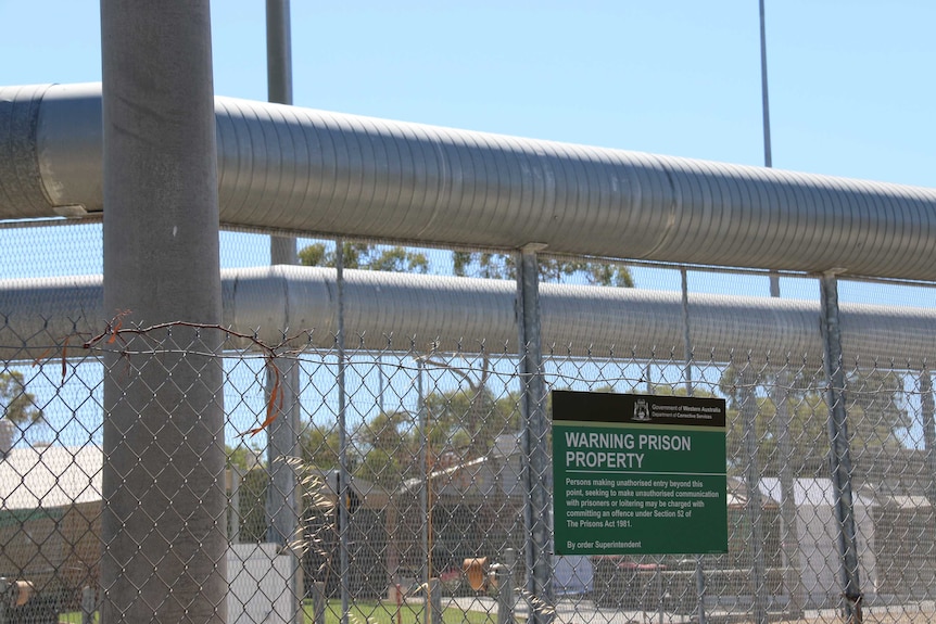 Security fencing outside Hakea Prison in Perth with a green 'Warning Prison Property' sign on the fence.