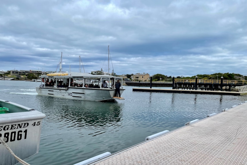 A small silver boat ferries cruise ship passengers into a marina.