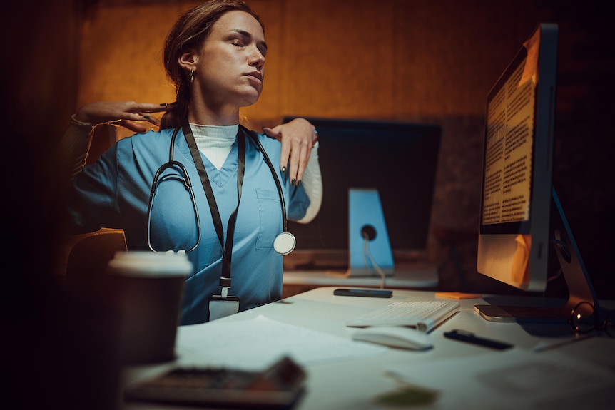 A nurse sits at the desk and working on a computer in a hospital office at night